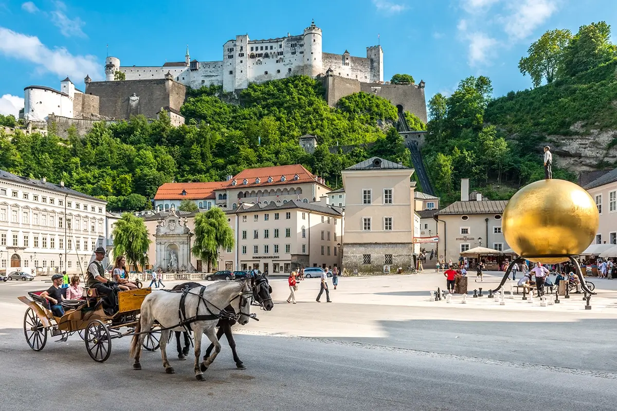 View of Residenzplatz in Salzburg with fiaker, palaces, sculpture, and Hohensalzburg, featured in the Salzburg travel bucket list.