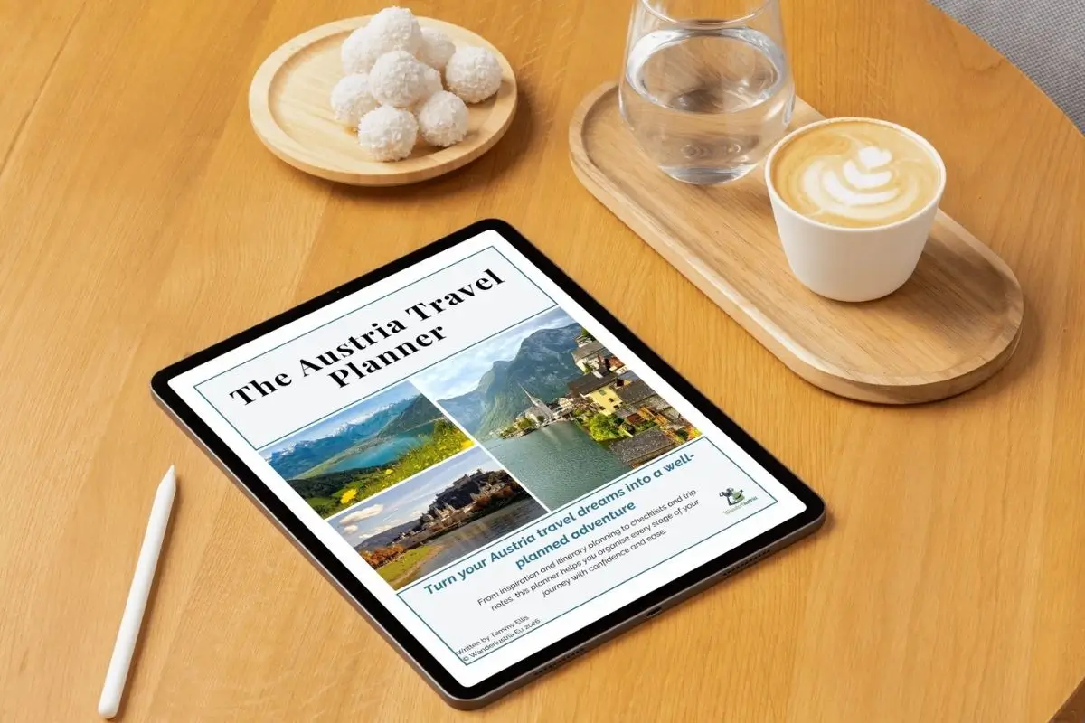 The Austria Travel Planner viewed on an iPad that is sitting on a wooden desk with a coffee next to it